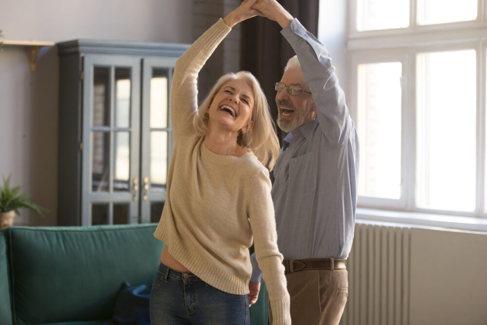 Overjoyed senior couple relax dancing at home