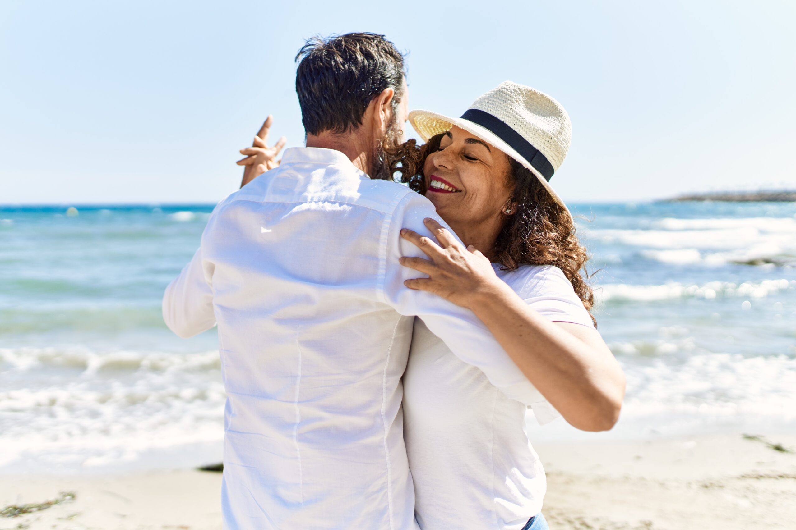 Middle age hispanic couple smiling happy dancing at the beach.