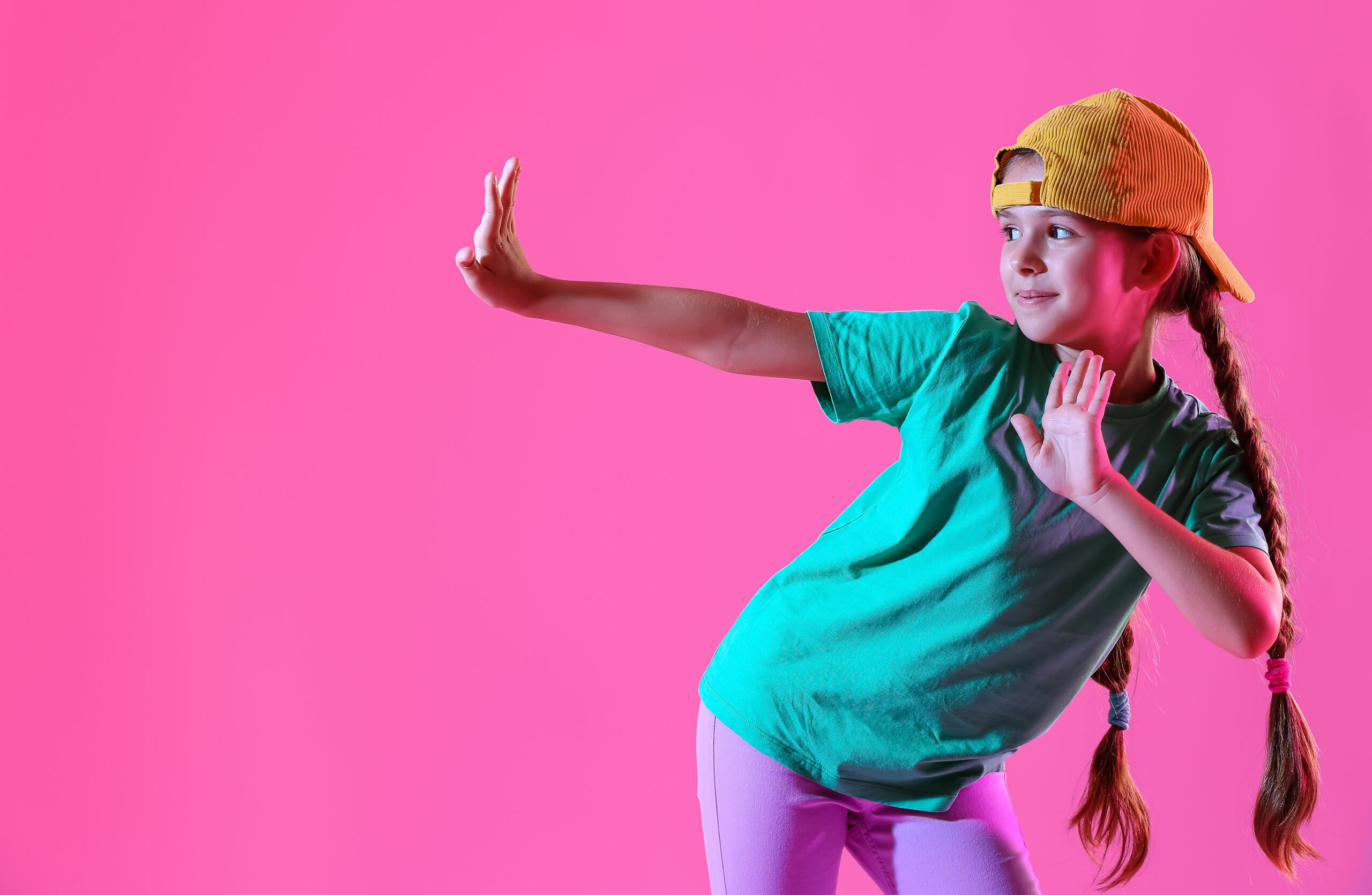 Cute little girl in cap dancing on pink background